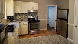 Una cocina compacta con armarios blancos, un refrigerador de acero inoxidable y una encimera de granito.