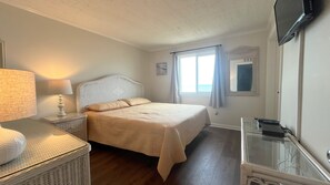 Une chambre à coucher avec un lit, des tables de chevet, une lampe, un téléviseur et une fenêtre avec des rideaux.