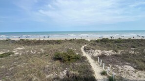 Una playa con un camino arenoso que lleva al agua, cielo despejado y el océano al fondo.
