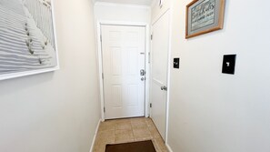 A hallway with a white door, a framed sign on the wall, and a doormat.