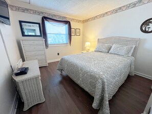 A bedroom with a bed, dresser, and a window with blinds.