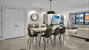 A modern living room with a dining area, a white couch, and a TV on the wall.