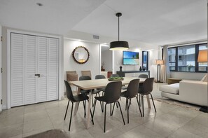 Uma sala de estar moderna com área de jantar, um sofá branco e uma TV na parede.