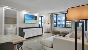 A modern hotel room with a bed, a desk, a sofa, a TV, and large windows.