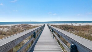 Ein hölzerner Steg führt zu einem Strand bei blauem Himmel.