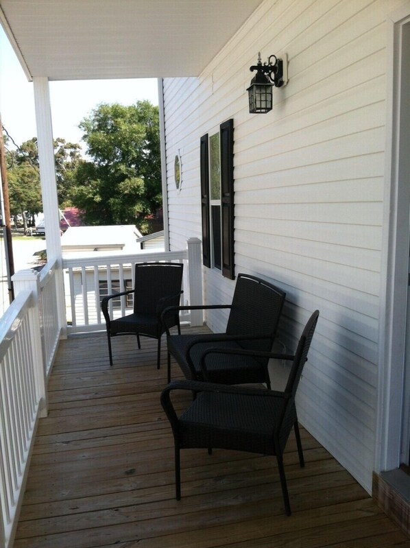 A covered porch with two chairs and a white railing.