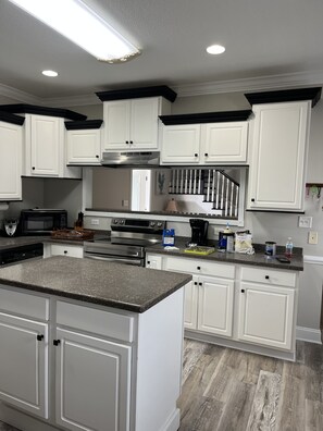 Una cocina moderna con armarios blancos, encimera de granito, electrodomésticos de acero inoxidable y salpicadero negro.