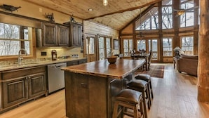 A spacious kitchen with a large island, wooden cabinets, and a dining area with a high ceiling and large windows. - Golden Oaks at Sugar Creek by Mountain Oasis | Luxury Blue Ridge Cabin Near Ellijay (Blue Ridge)