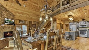 A rustic wooden interior with a fireplace, dining table, and kitchen area. - Golden Oaks at Sugar Creek by Mountain Oasis | Luxury Blue Ridge Cabin Near Ellijay (Blue Ridge)
