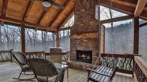 A covered outdoor area with a stone fireplace, wooden flooring, and seating. - Golden Oaks at Sugar Creek by Mountain Oasis | Luxury Blue Ridge Cabin Near Ellijay (Blue Ridge)