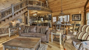 A spacious log cabin interior with a central living area, a dining area, and a kitchen. - Golden Oaks at Sugar Creek by Mountain Oasis | Luxury Blue Ridge Cabin Near Ellijay (Blue Ridge)