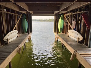 Un muelle de madera que se adentra en una masa de agua tranquila, con dos tablas de surf apoyadas contra las paredes.