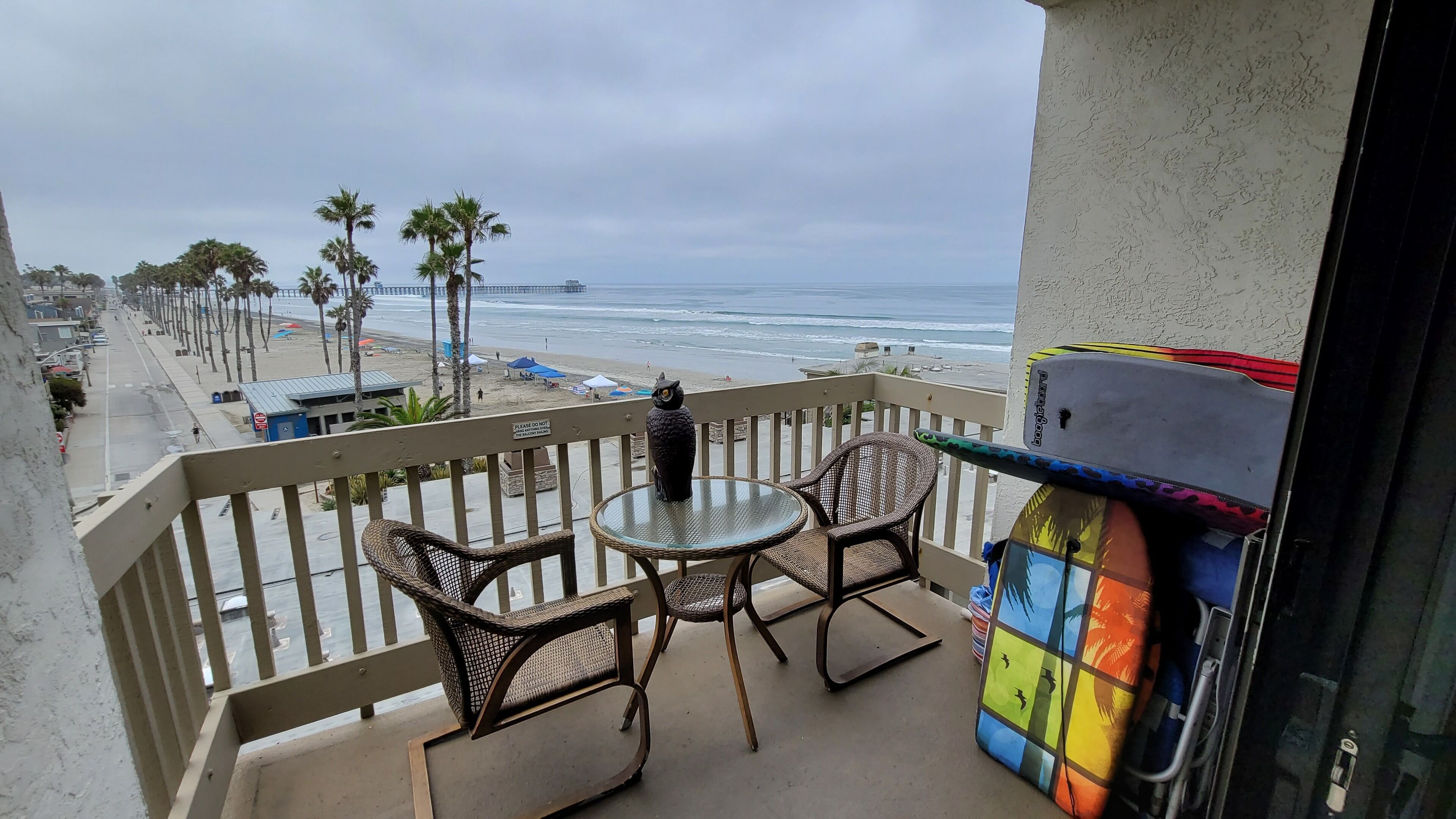 Un balcon avec des fauteuils en osier et une table, donnant sur une plage bordée de palmiers et sur l’océan.