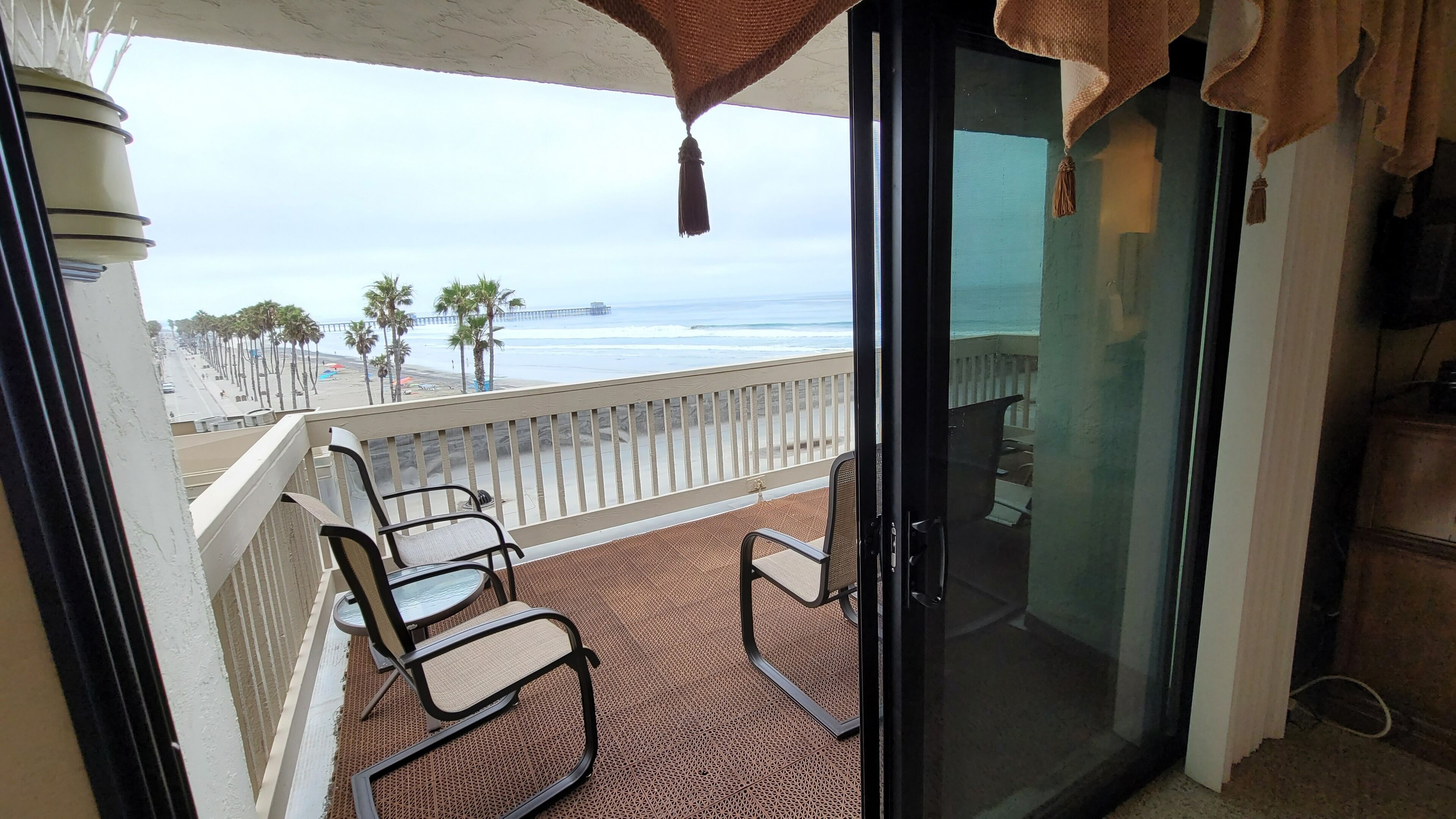 Ein Balkon mit zwei Stühlen und einer Glastür, die Blick auf einen Strand bietet.
