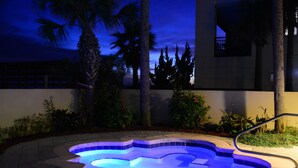 Ein Pool mit ungewöhnlicher Form, umgeben von Palmen und einem Gebäude im Hintergrund.