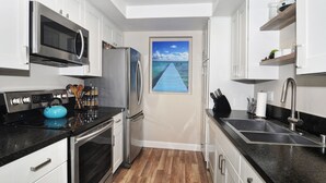Une cuisine moderne dotée d’appareils électroménagers en acier inoxydable, d’un plancher en bois et offrant une vue sur une jetée, visible à travers une porte.