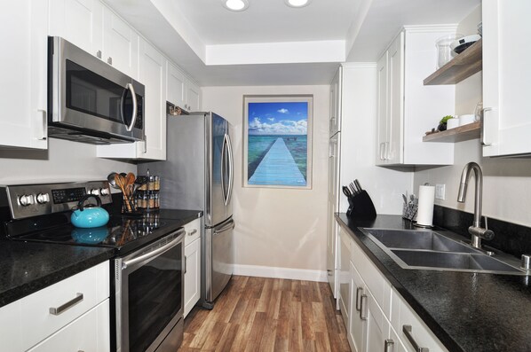 A modern kitchen with stainless steel appliances, a wooden floor, and a view of a pier through a door.