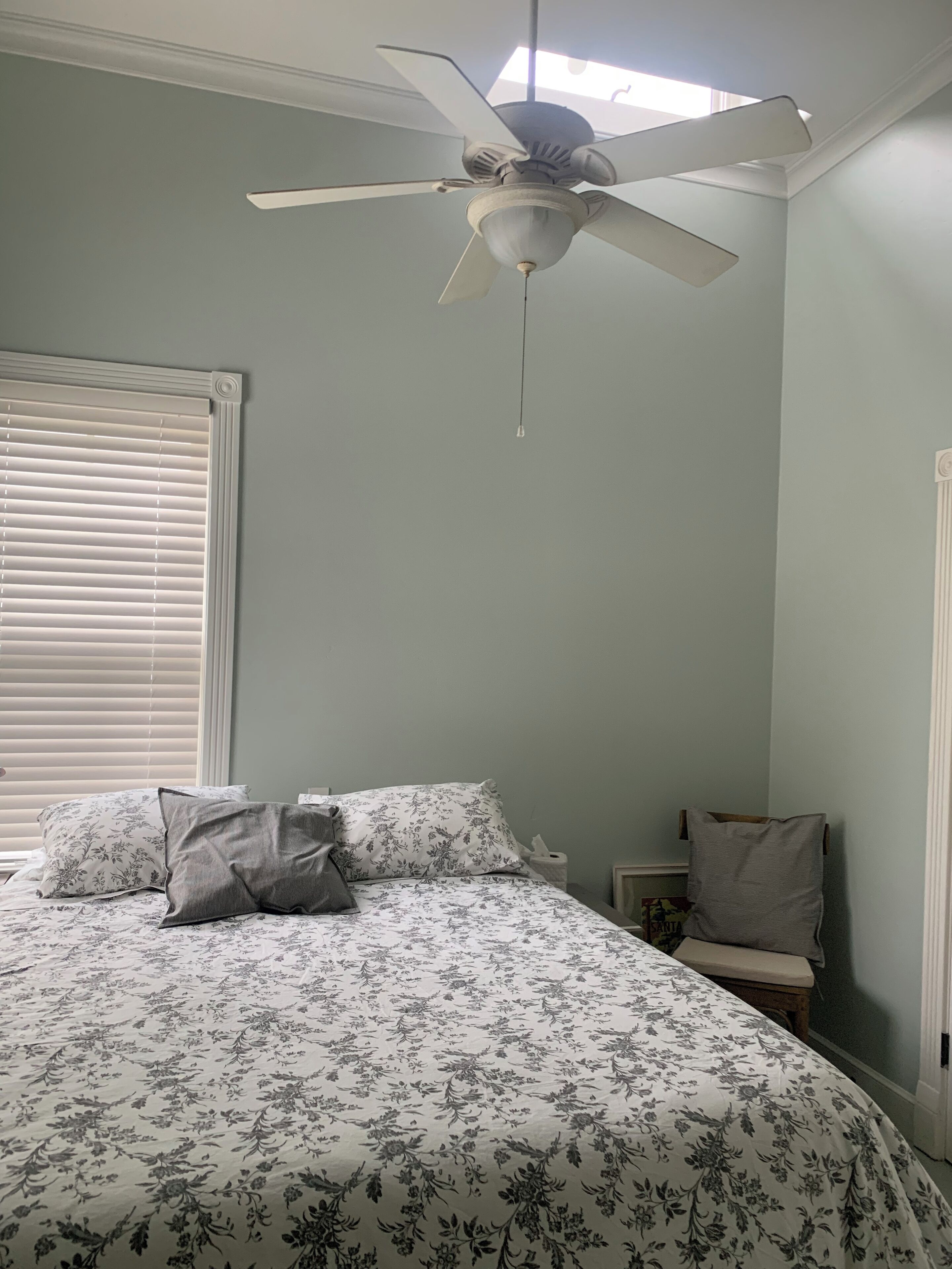 Une chambre à coucher avec un lit, un ventilateur de plafond, une table de chevet et une fenêtre avec des stores.