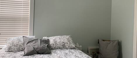 Une chambre à coucher avec un lit, un ventilateur de plafond, une table de chevet et une fenêtre avec des stores.