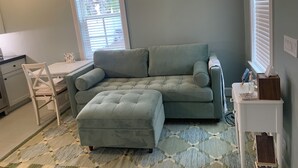 Une pièce confortable avec un canapé gris, un petit pouf, un bureau blanc et une chaise.