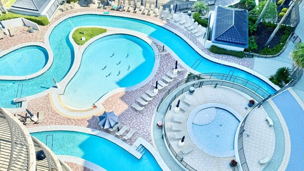Un gran complejo turístico con múltiples piscinas, zonas de descanso con tumbonas y una piscina circular central.