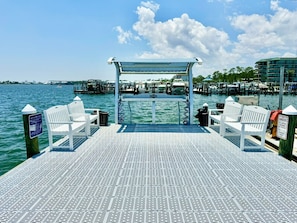 A pier with white chairs and a covered area, overlooking a marina with boats and buildings.