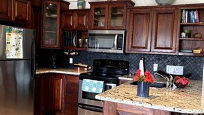 Una cocina con armarios de madera, un refrigerador de acero inoxidable, un microondas, un horno, una encimera de granito y un taburete de bar.