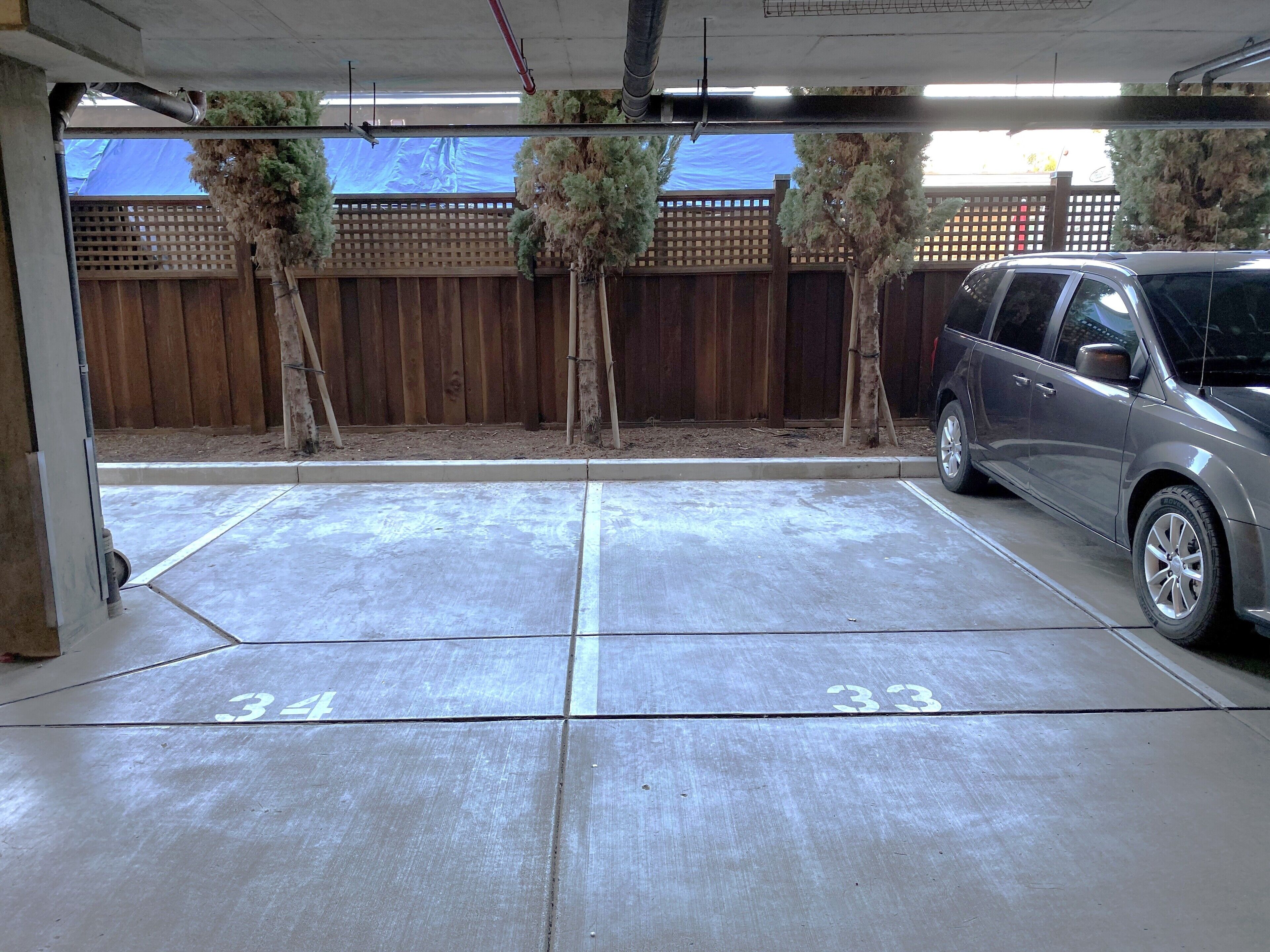 Un garaje para estacionamiento con pisos de concreto, espacios delimitados y una valla de madera al fondo.