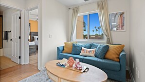 Una sala de estar con un sofá azul, una mesa de centro de madera y vistas a palmeras a través de una ventana.
