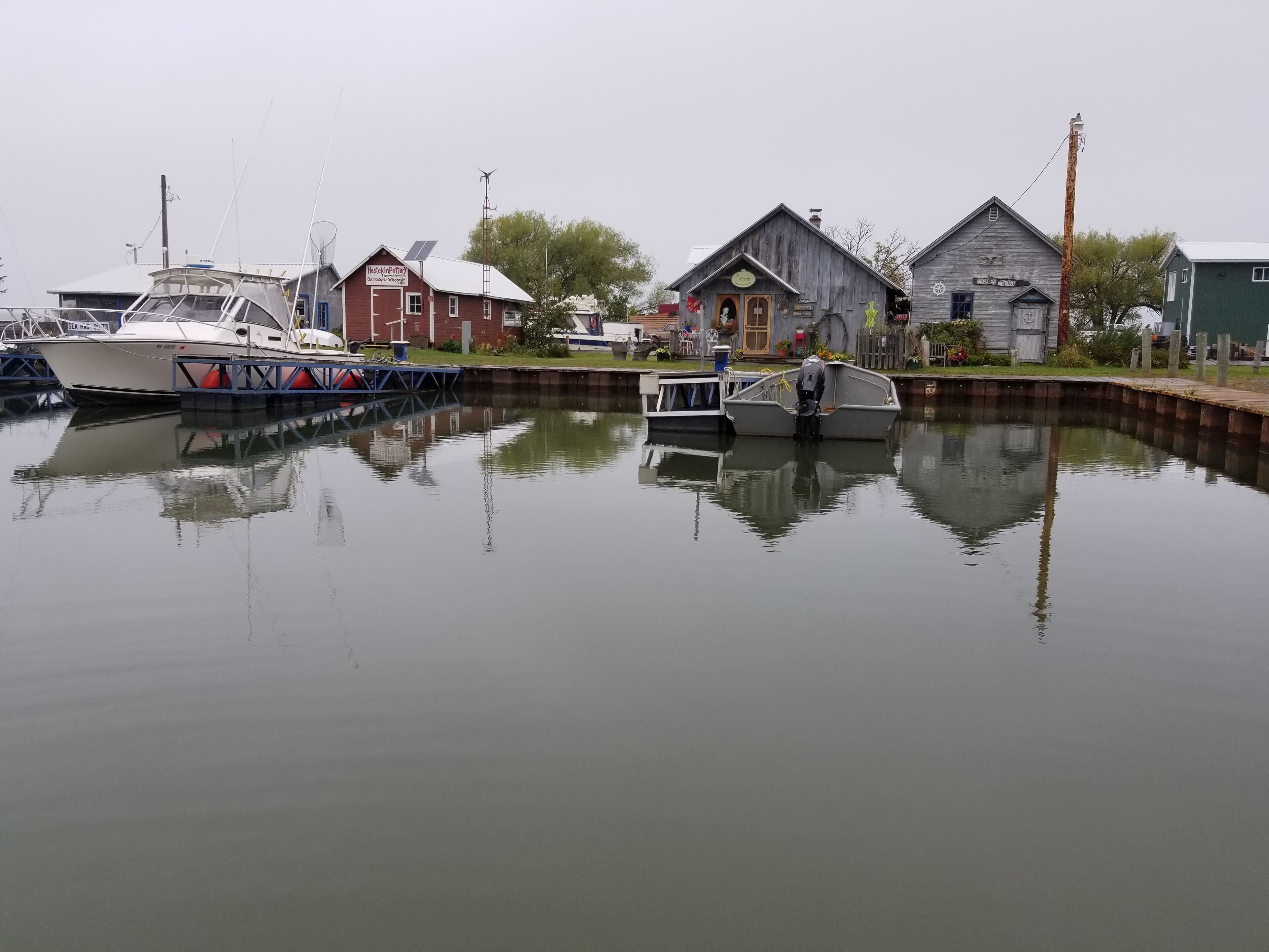 A calm waterfront with a docked boat, a small house with a sign, and another building with a sign.