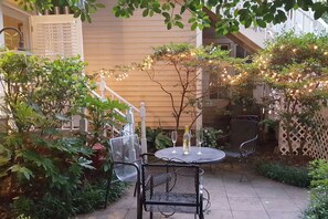 Eine Terrasse mit rundem Tisch und Stühlen, umgeben von Grünpflanzen und Lichterketten.