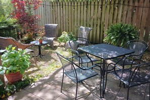 Eine Terrasse mit einem Metalltisch und -stühlen, umgeben von Kübelpflanzen und einem Holzzaun.