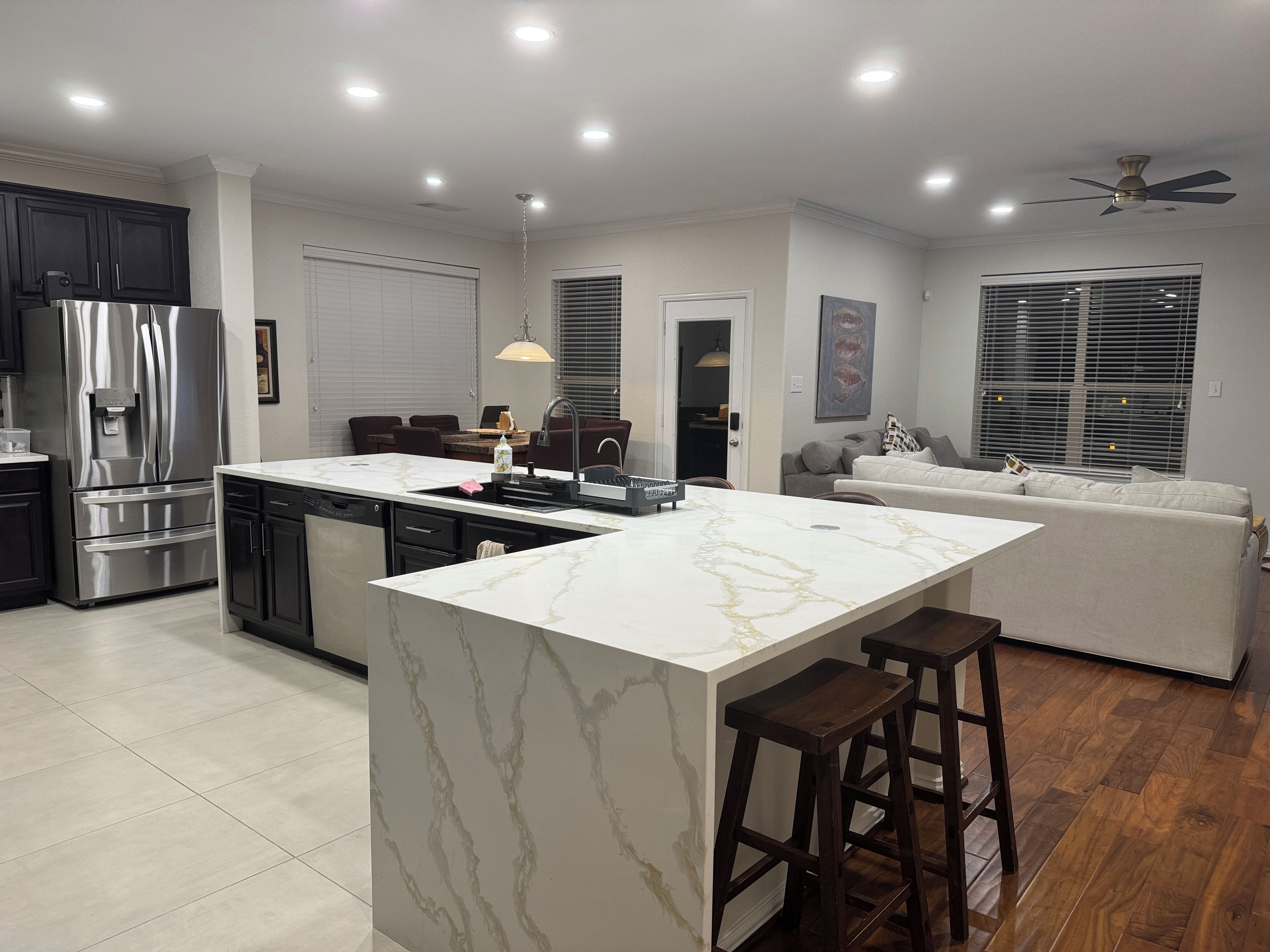 A modern kitchen with a central island, stainless steel appliances, and a dining area with a sofa and bar stools.