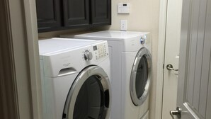 A laundry room with two front-loading washing machines, a dark wooden cabinet above, and a white door to the right. - Nice Family Friendly, WalMart and HEB & Wallgreens Walking, Iron Man. (The Woodlands)