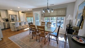 A spacious kitchen with modern appliances, a dining area with a large table and chairs, and a view of the outdoors through a sliding glass door. - Pet-Friendly 3BR Inlet Cove Cottage - Walk to Beach, Pool & Kiawah River (Johns Island)