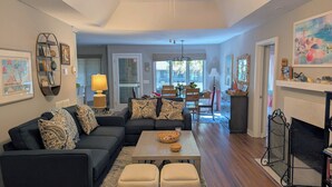 A living room with a dark-colored sofa, patterned cushions, a wooden coffee table, and a fireplace. - Pet-Friendly 3BR Inlet Cove Cottage - Walk to Beach, Pool & Kiawah River (Johns Island)
