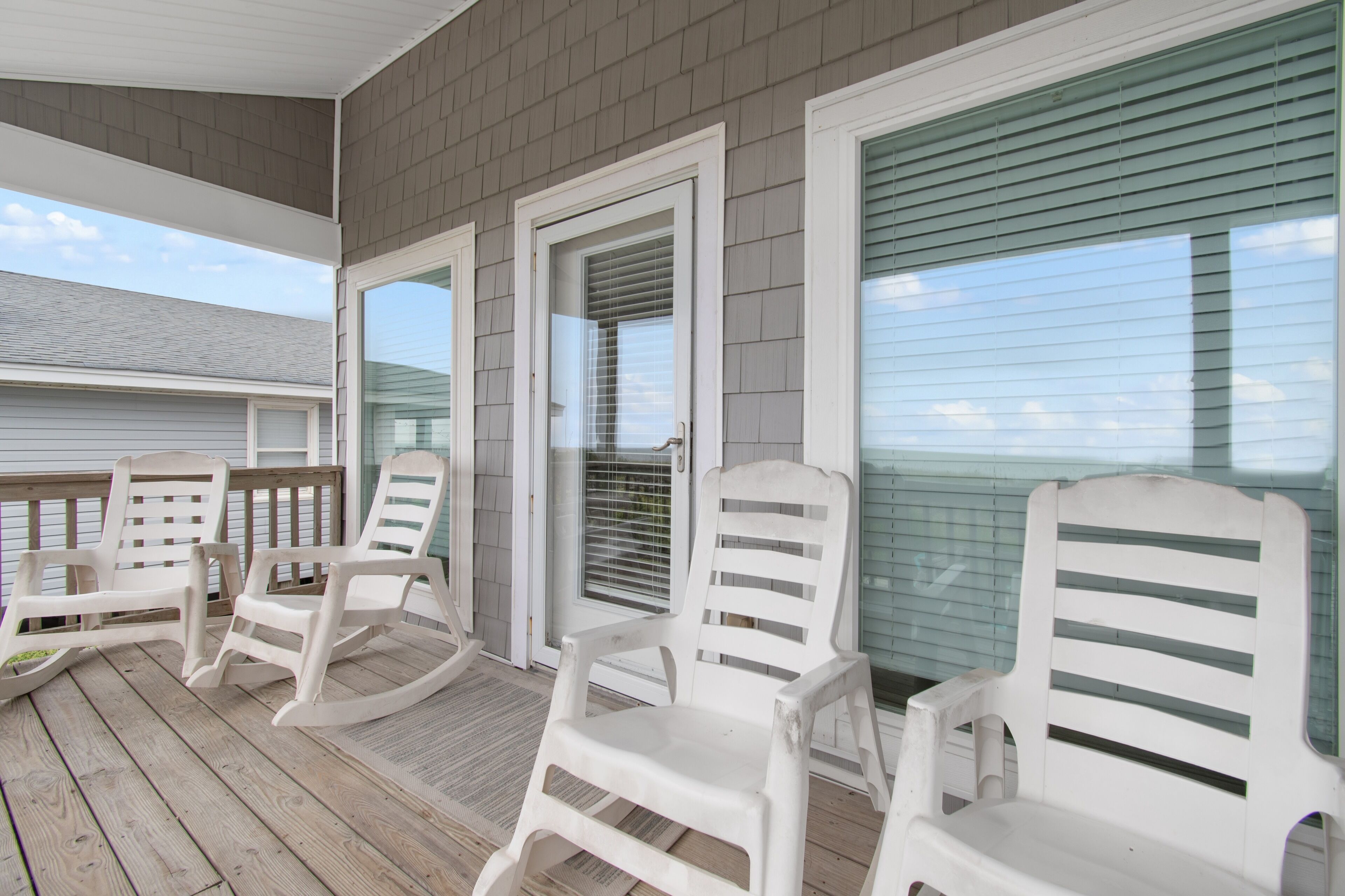 A covered porch with white rocking chairs and a wooden deck.