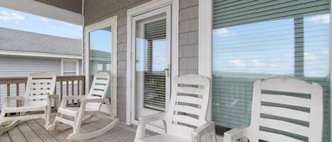 A covered porch with white rocking chairs and a wooden deck.