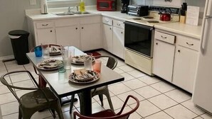 A compact kitchen with white cabinets, a dining table with chairs, and a tiled floor.