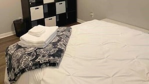 A bedroom with a bed, a black storage unit with white drawers, a ceiling light, and a window with blinds.
