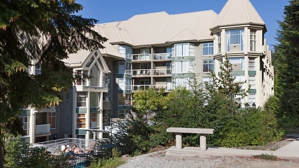 A multi-story building with balconies, a pool area, and a stone bench. - Carv'em or Park'em at Our Ski-in/Ski-out Condo in Woodrun (Whistler)