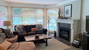 A living room with a sofa, ottoman, fireplace, and a television. - Carv'em or Park'em at Our Ski-in/Ski-out Condo in Woodrun (Whistler)