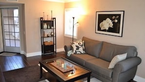A living room with a grey sofa, a coffee table, a bookshelf, and a framed picture on the wall. - Beach Walk to Salt Creek Beach for Surf and Sun - Air Conditioned STR15-0392 (Dana Point)
