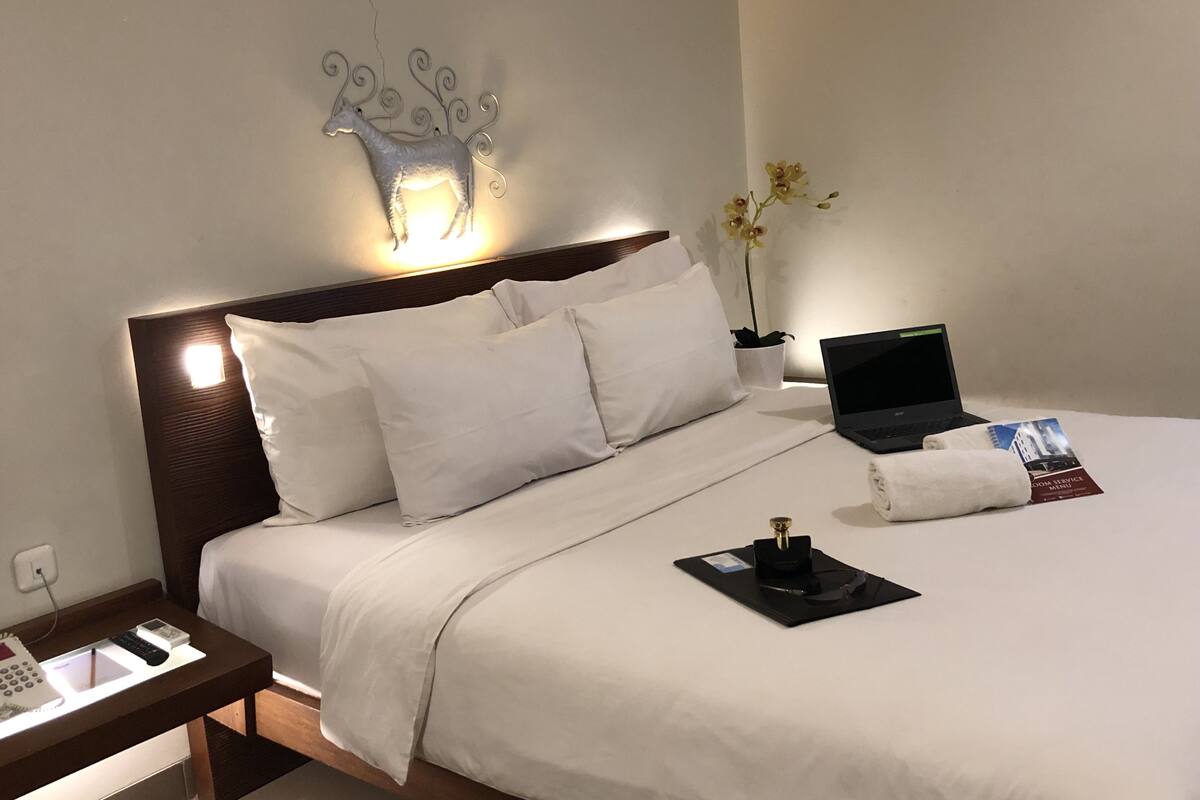A neatly made bed with white linens, a laptop, a small potted plant, and a decorative wall piece.