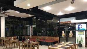 Un restaurante con mesas y sillas de madera, un escenario y una pantalla de televisión.
