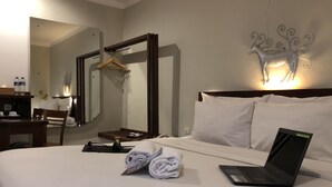 Habitación de hotel con cama, ordenador portátil, toallas enrolladas, espejo, perchero y un ciervo decorativo en la pared.