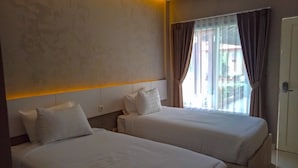 Une chambre d’hôtel avec deux lits, une grande fenêtre avec des rideaux et une tête de lit moderne.