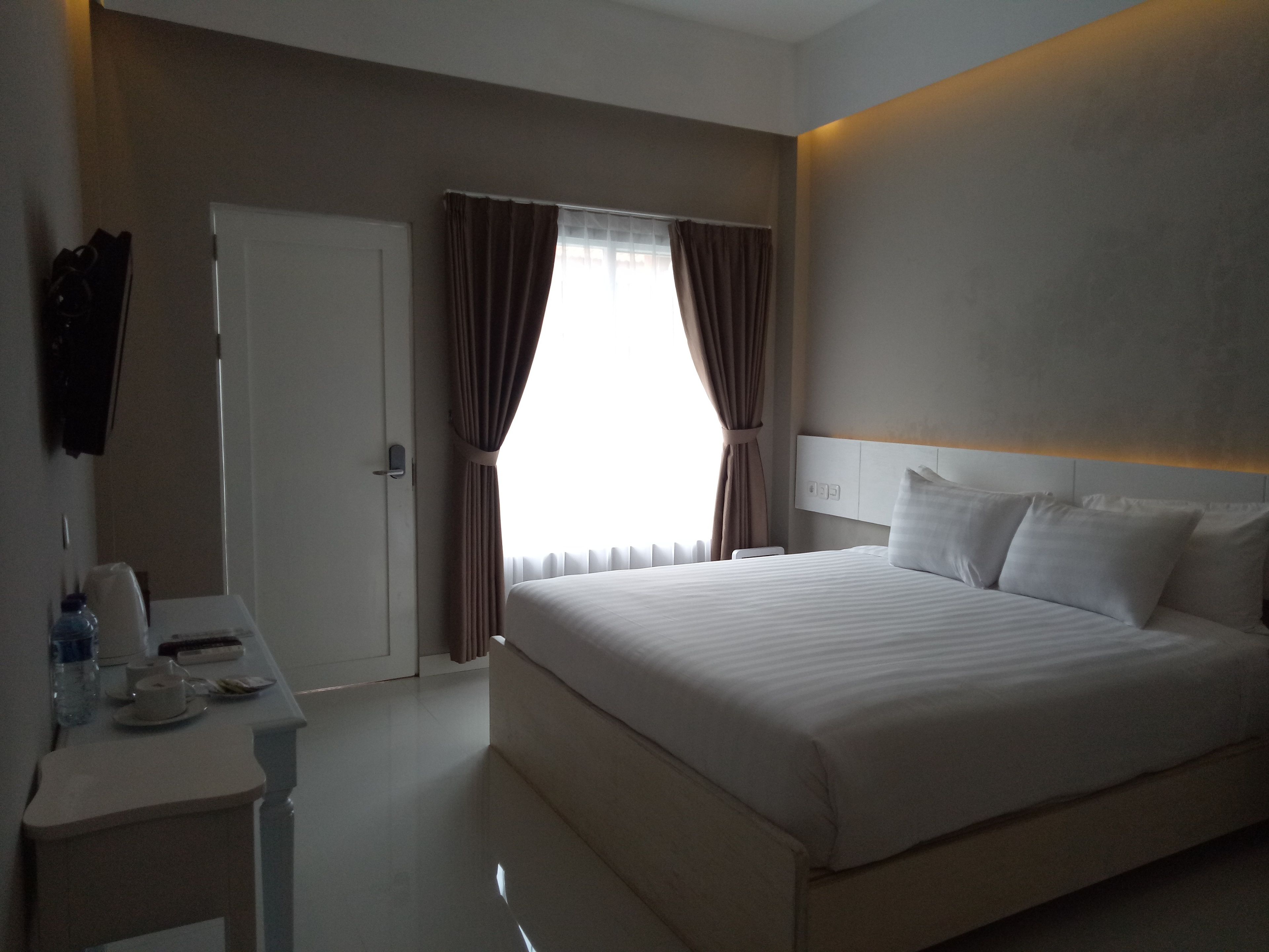 A hotel room with a bed, bedside table, and a window with curtains.