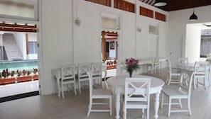 A spacious dining area with white furniture and a view of a pool.