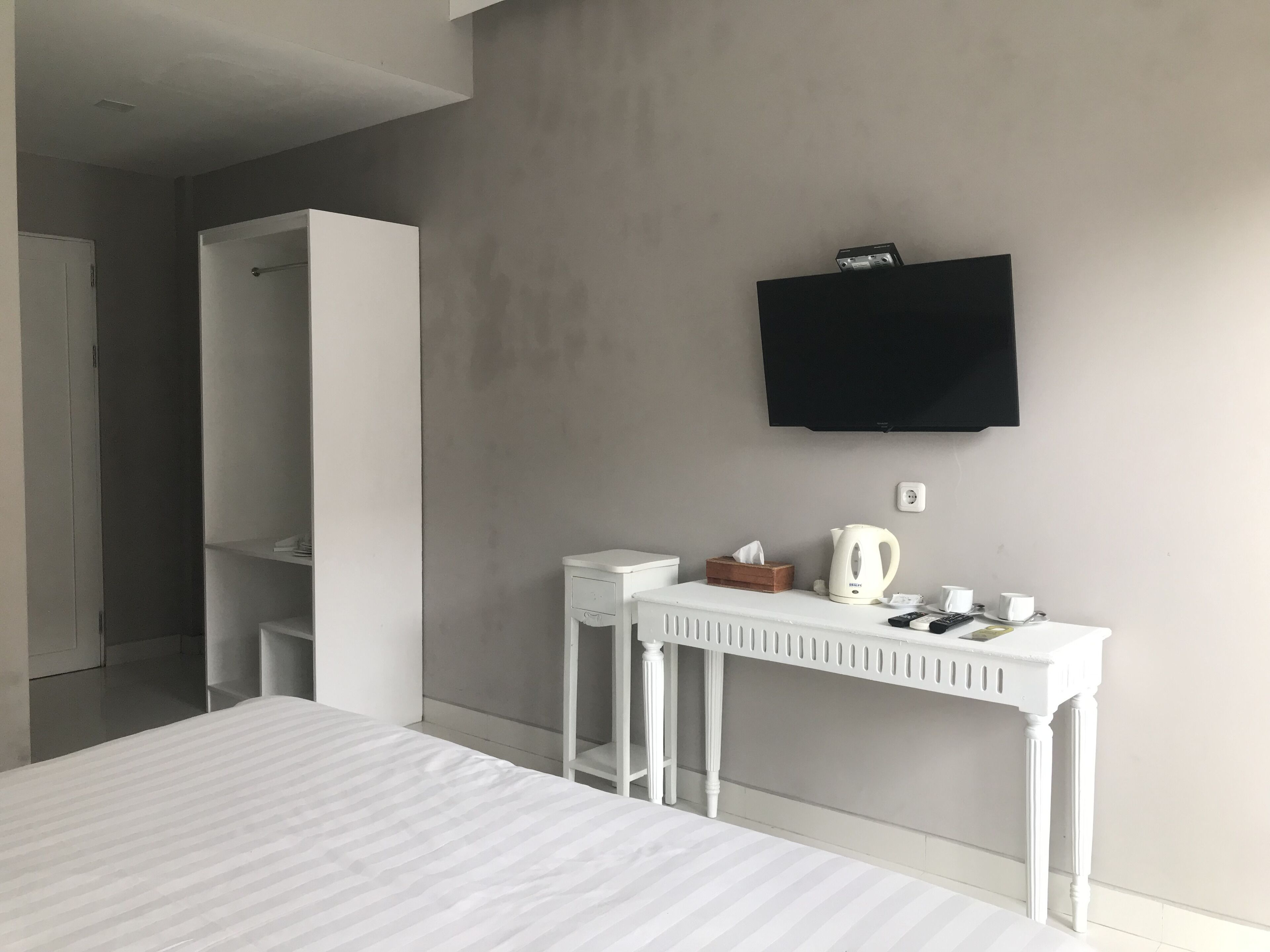 A modern hotel room with a bed, a white desk, a television, and a wardrobe.
